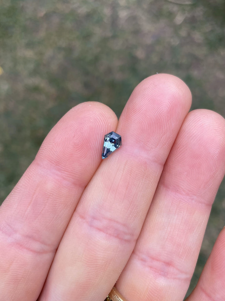 A 1.13-carat sapphire with an opalescent denim blue hue resting on the fingertip, highlighting its stunning step cut shield shape and reflecting light beautifully. The gem is no-heat treated and sourced from Madagascar.