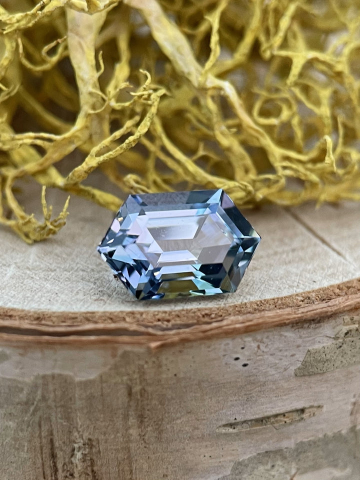 Close-up of a 2.08-carat mermaid Tanzanite gemstone in a hexagonal step cut, showcasing a mesmerizing blend of teal, blue, and violet hues, set on a natural wooden background.