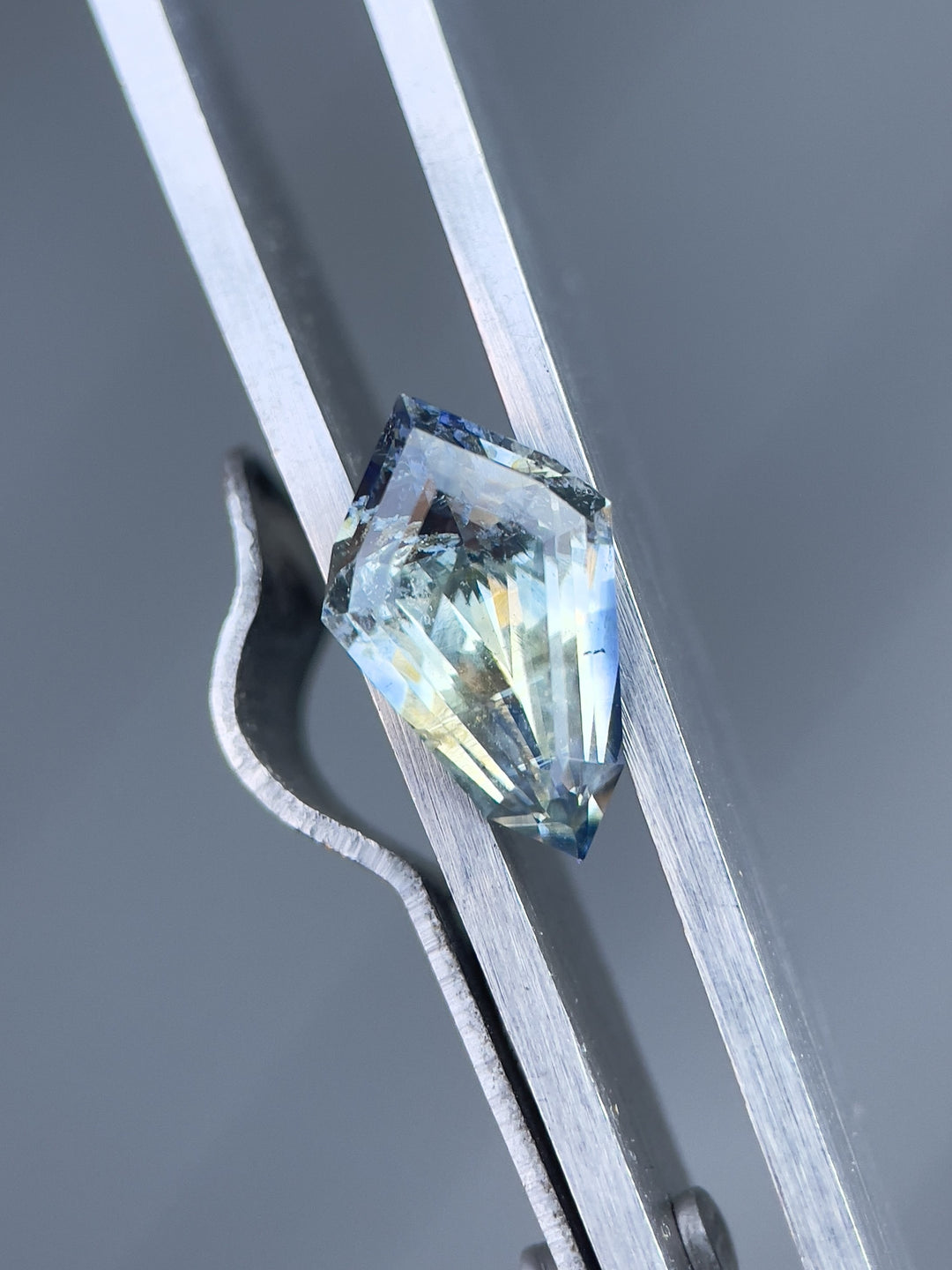 Stunning 2.32 carat no-heat sapphire, showcasing a geometric step cut kite shape, primarily yellow with Ceylon denim hues, captured in precision grip, origin Sri Lanka, dimensions 11.90 x 7.43 x 4.46 mm.