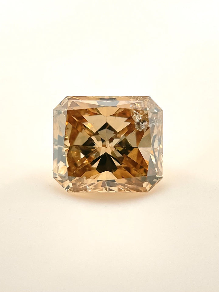Radiant cut 3.68-carat champagne diamond resting on a white background, displaying its impressive color and step-cut reflections.