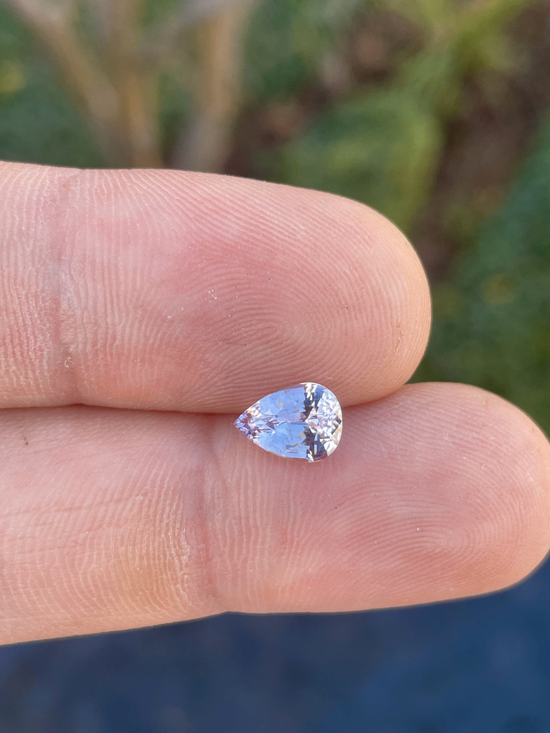 A side view of a pastel pink and purple 1.68-carat sapphire, in a pear cut with a glossy finish. This Sri Lankan gemstone is untreated and unique.