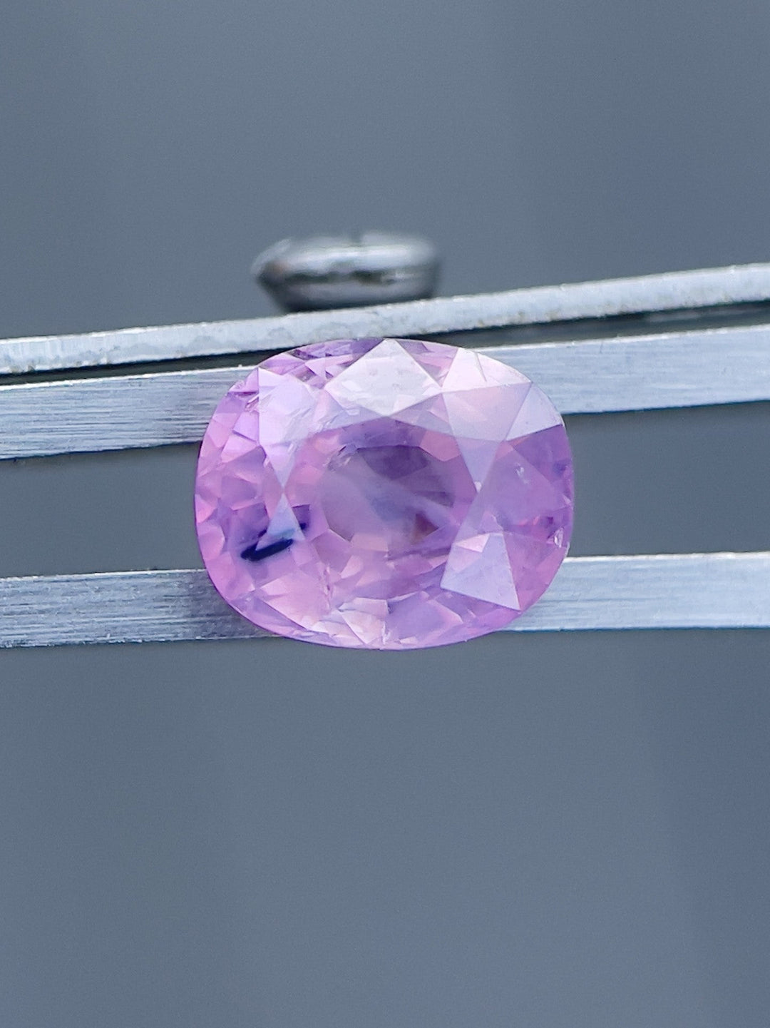 Captivating 1.77ct pink and purple opalescent sapphire from Luc Yen, Vietnam, showcased in a mix cushion cut, measuring 7.53 x 6.13 x 4.42 mm, displayed in metal clamps against a gray background.