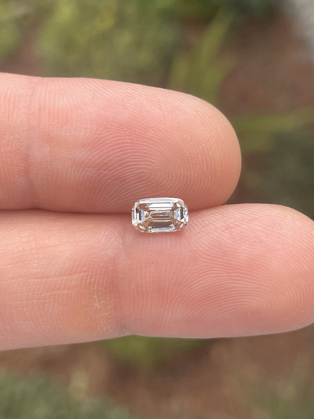 A 1.03-carat vintage cushion-cut diamond resting on a fingertip, highlighting its warm champagne hue and elegant elongated step-cut facets.