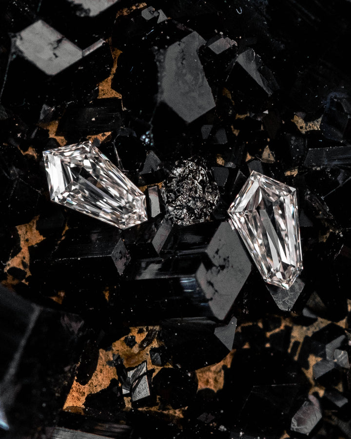 Matched 0.10ct F-G color VVS-VS clarity kite step cut diamonds displayed on raw black crystal matrix, showcasing their sharp geometric faceting and brilliance; ethically sourced untreated diamonds from South Africa.