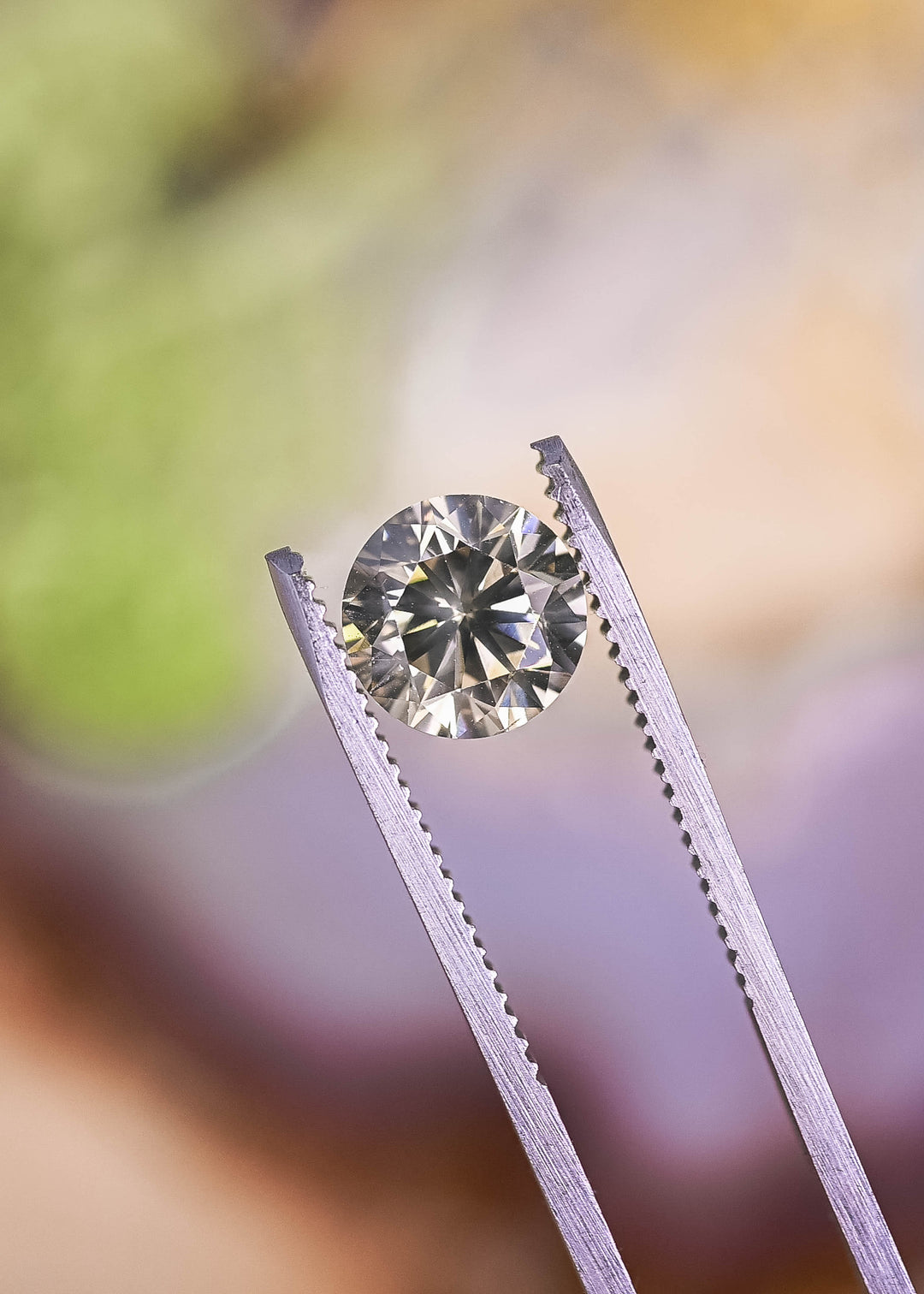 Loose VVS1 fancy yellow brown diamond held in tweezers displaying round cut brilliance and natural champagne color.