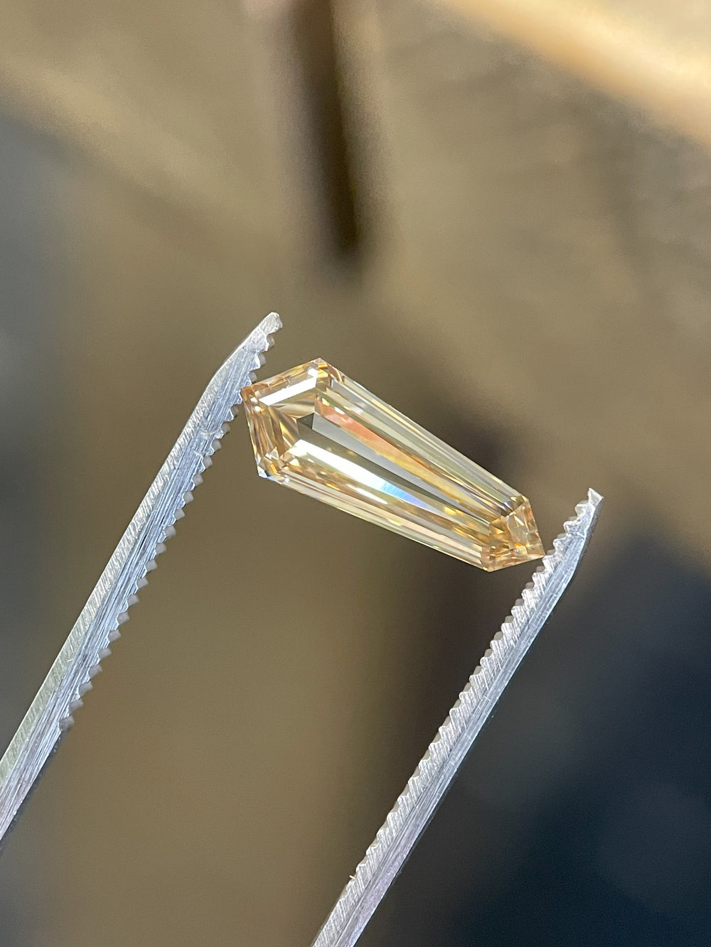 Fancy brown 2.02-carat champagne diamond held in precision tweezers, showcasing its sharp step-cut facets and clarity.