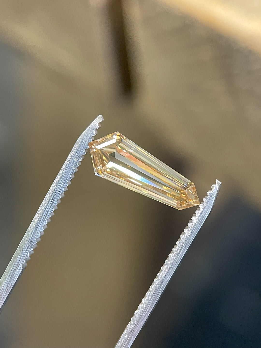 Fancy brown 2.02-carat champagne diamond held in precision tweezers, showcasing its sharp step-cut facets and clarity.