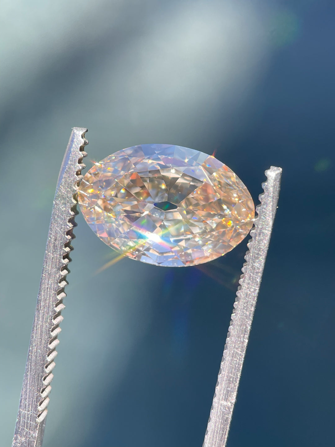 A dazzling 3.01-carat antique moval cut diamond with fancy light brown champagne hues, held in precision tweezers under natural light, reflecting stunning rainbow fire and brilliance.