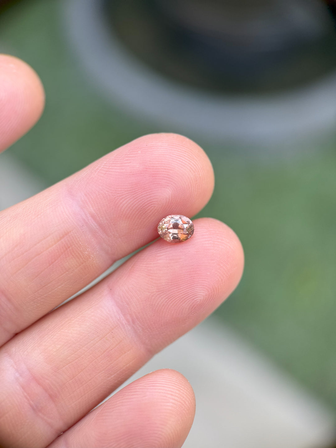 Close-up image showing scale of a natural 0.95ct color-shift peach pink sapphire in fingers, untreated and sourced from Umba River, Tanzania.