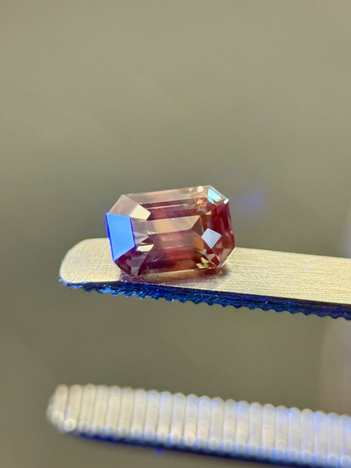 Close-up of a 1.60 carat sapphire in an emerald cut, capturing its earthy parti colors under lighting—set against tweezers.