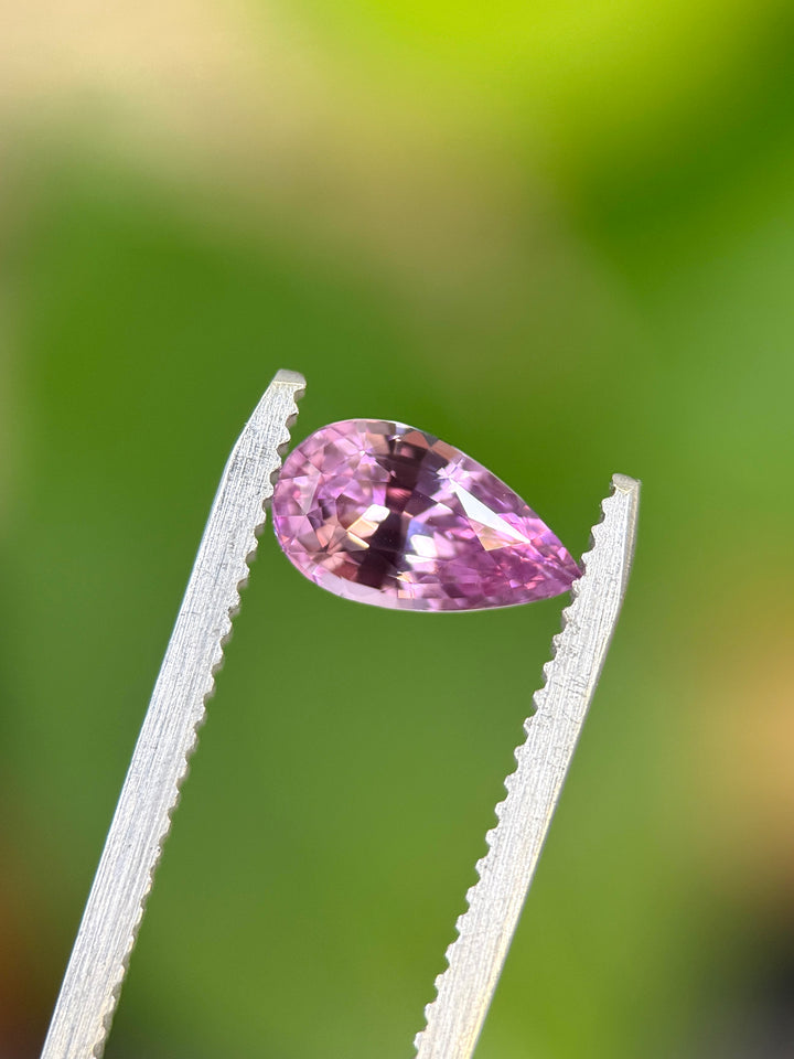 Purple gemstone held by tweezers against a blurred green background