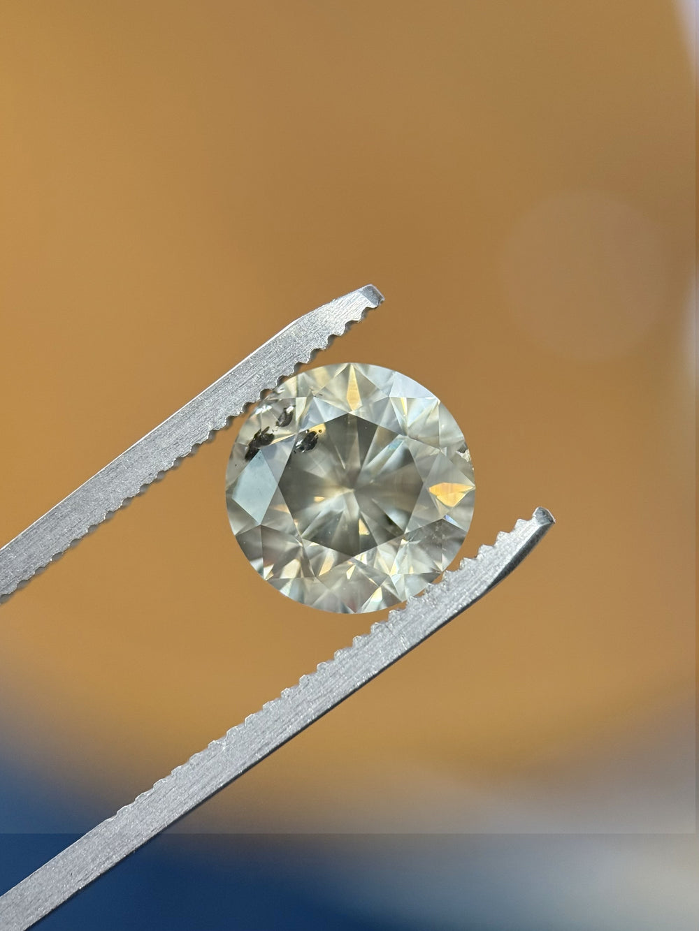 Macro image of 3.99CT Fancy Dark Gray round brilliant cut diamond held with tweezers against warm lighting to highlight sparkle, luster, and clarity characteristics.