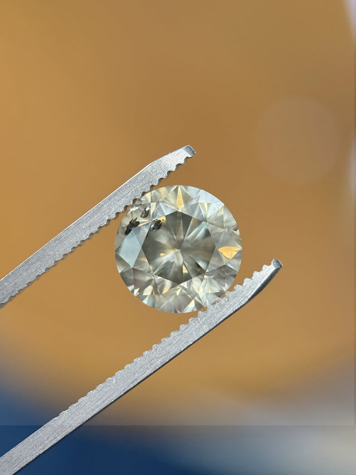 Macro image of 3.99CT Fancy Dark Gray round brilliant cut diamond held with tweezers against warm lighting to highlight sparkle, luster, and clarity characteristics.
