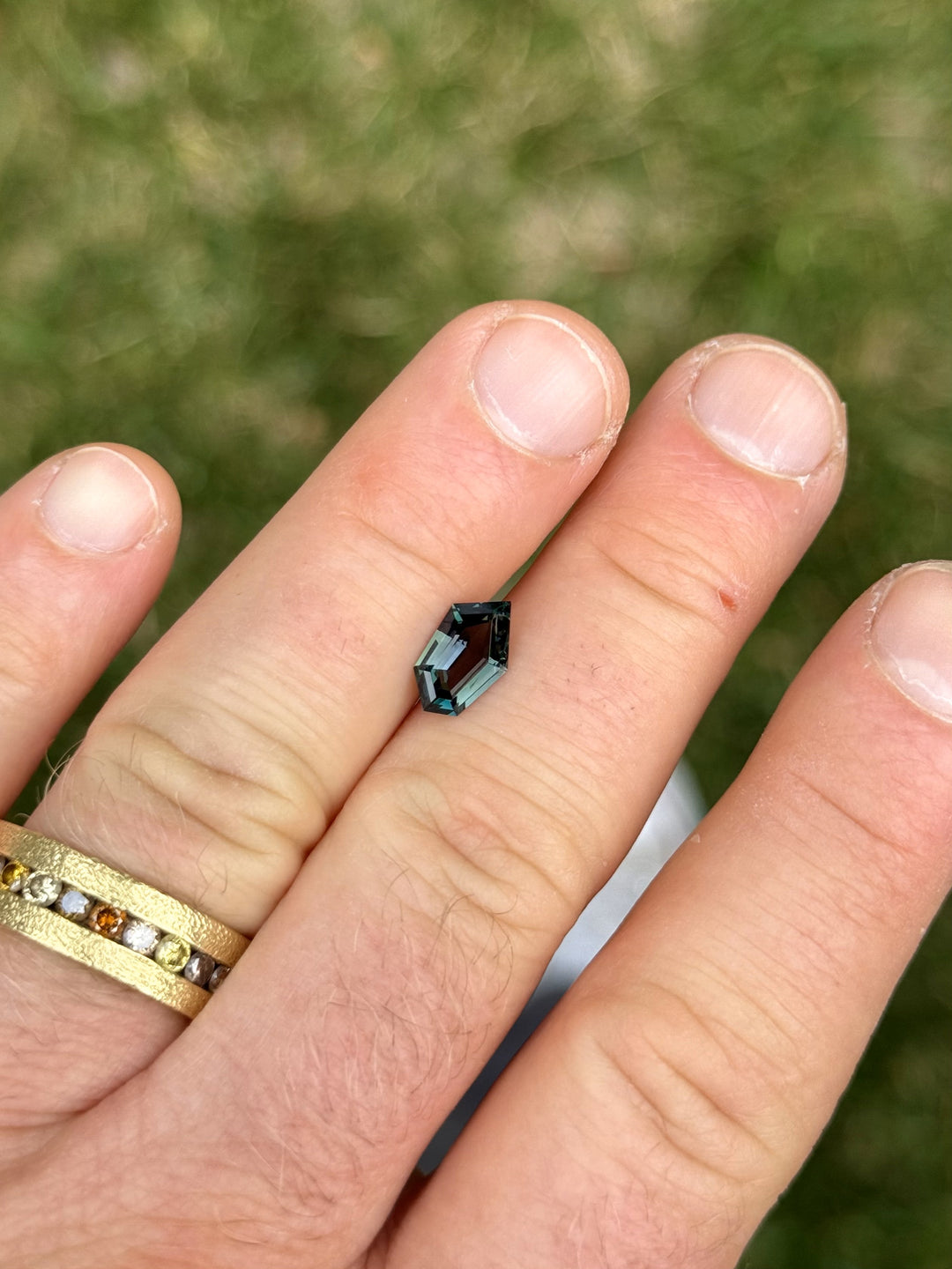Close-up of a 1.55 carat green tanzanite gemstone held between fingers, showcasing its custom geometric freeform step cut and deep saturation