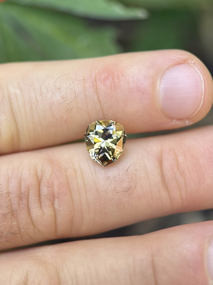 Fancy colored Tanzanite weighing 3.25 carats displayed on fingers to show scale. Featuring a geometric pear mixed brilliant cut with natural lavender and golden tones.