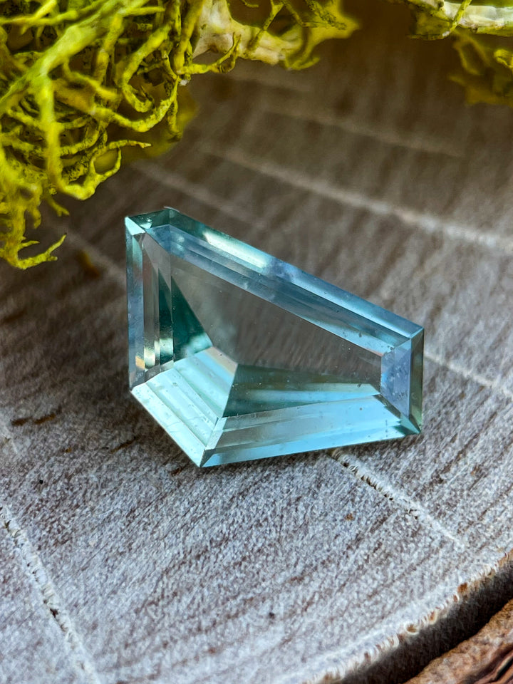 A stunning 2.00-carat sapphire featuring a freeform geometric cut, showcasing a blend of blue and green colors, displayed on a textured surface.