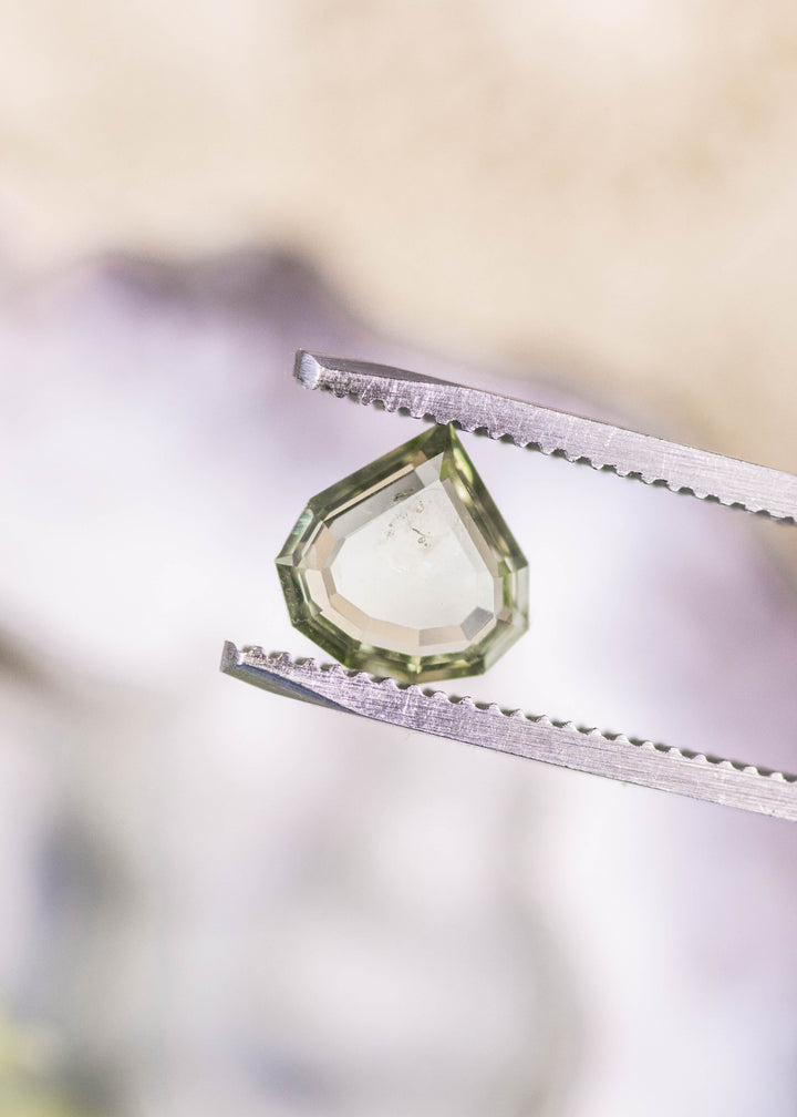 1.75 carat untreated Montana sapphire held in gem tweezers, highlighting teal yellow green color zoning and precise geometric step cut portrait pear facets