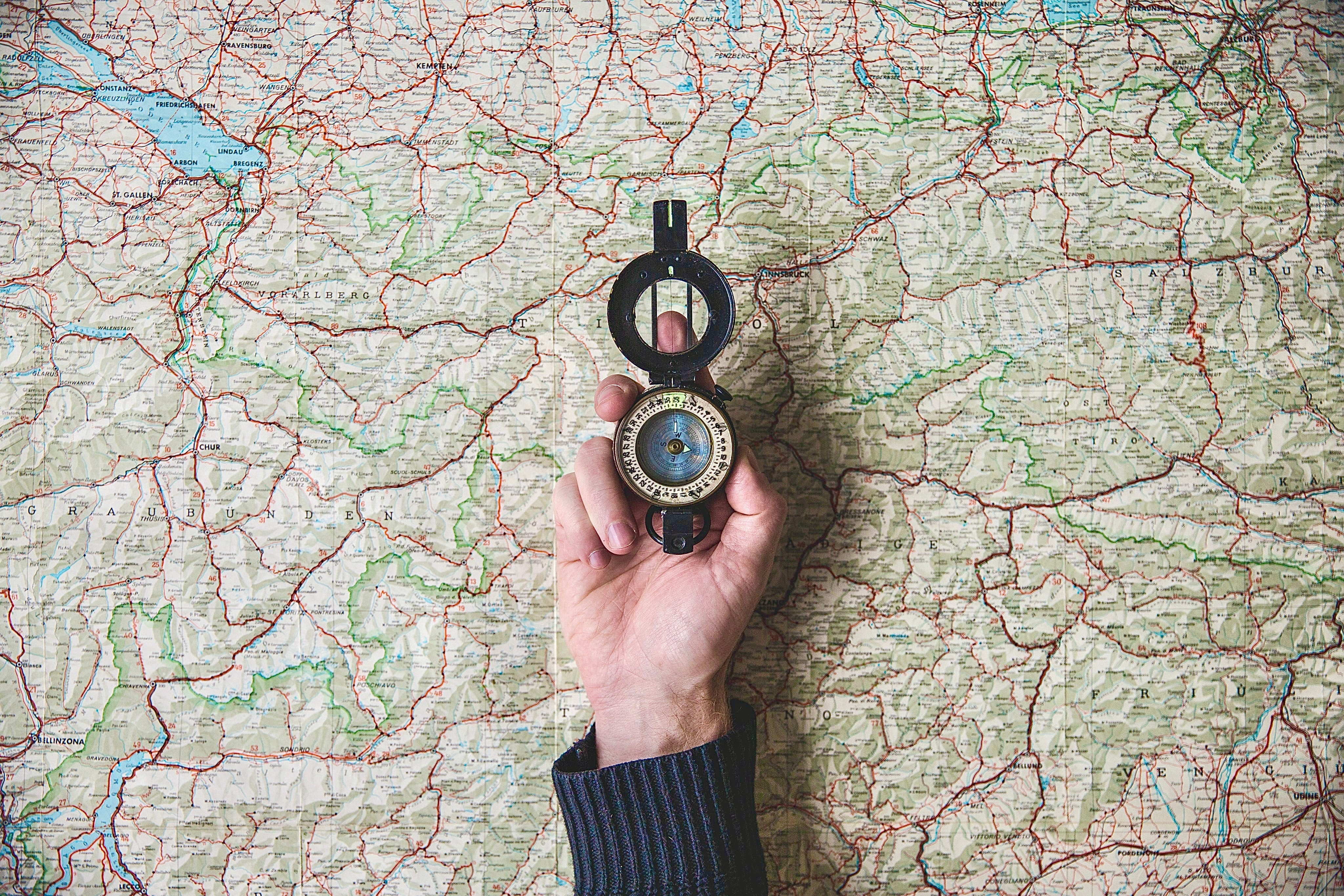 Hand holding a compass over a world map, representing global gemstone sourcing and the search for rare natural loose gemstones.