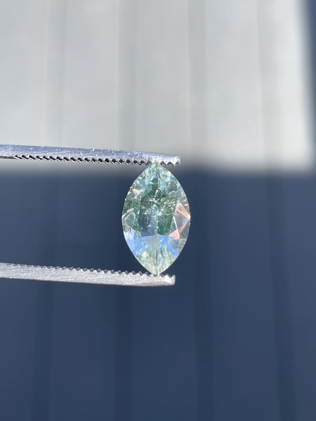 A natural 2.18ct Hyalite Opal in oval brilliant cut, held in gem tweezers against a bright background.