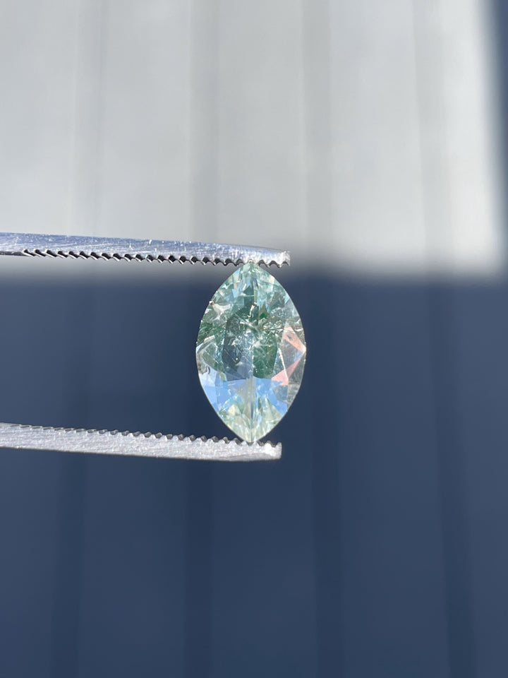 A natural 2.18ct Hyalite Opal in oval brilliant cut, held in gem tweezers against a bright background.