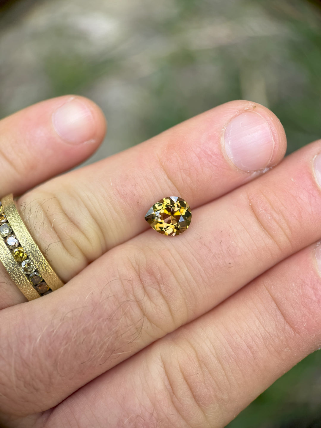 2.17 carat tanzanite gemstone held between fingers, showcasing peach and golden yellow color with modified brilliant poval cut