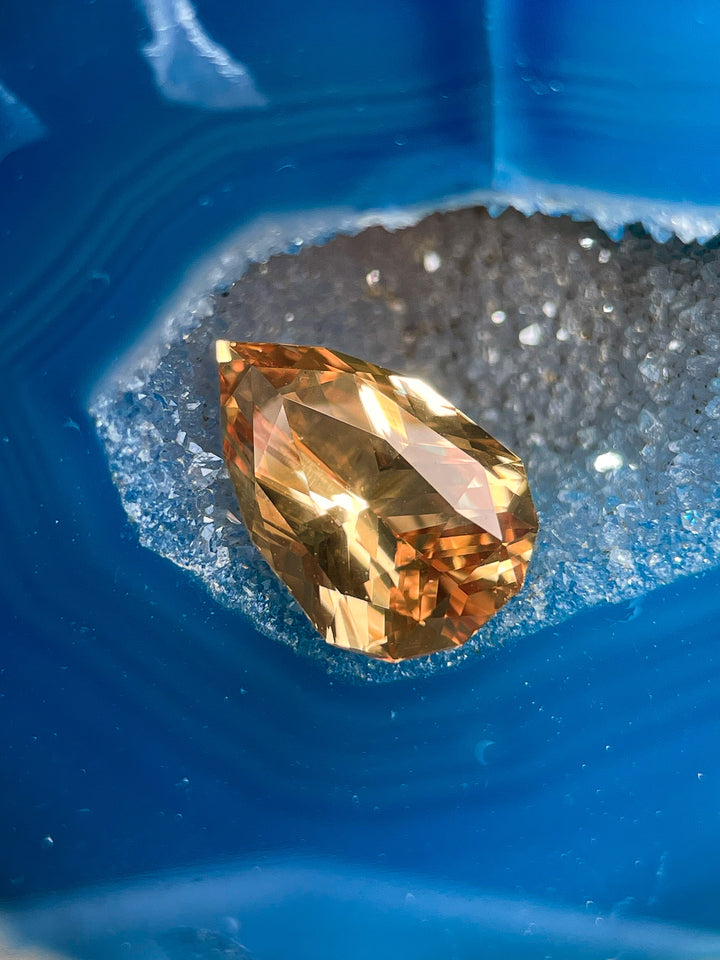Yellow-Brown Sapphire resting on a vivid blue geode, displaying its unique mix brilliant pear cut and captivating color.