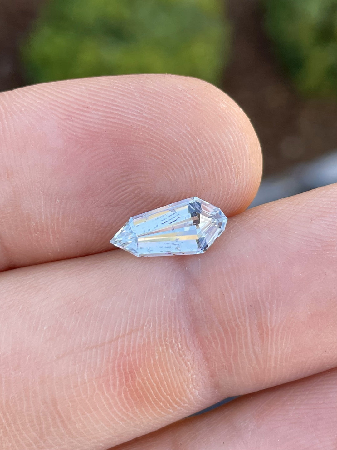 A 1.90-carat pale seafoam sapphire in a custom step cut shield shape, delicately balanced on a fingertip, showcasing its clarity, elongated facets, and no-heat treatment.