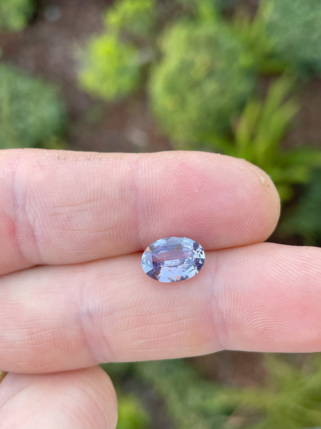 A close-up view of a 2.56 carat purple oval-cut sapphire placed on the fingers for scale, showcasing its brilliance and natural origin from Sri Lanka.