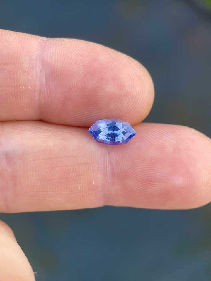 Close-up of a 1.73 carat parti sapphire resting on a finger, showcasing its unique denim blue and cornflower coloration and custom geometric marquise cut, sourced from Sri Lanka.
