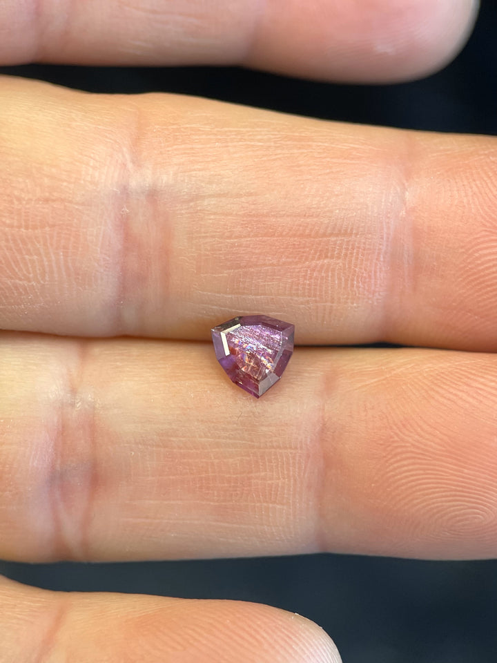 A 1.10-carat ruby with red and purple hues in a custom trillion cut, resting on a person's fingers. Origin: Umba River, Tanzania.