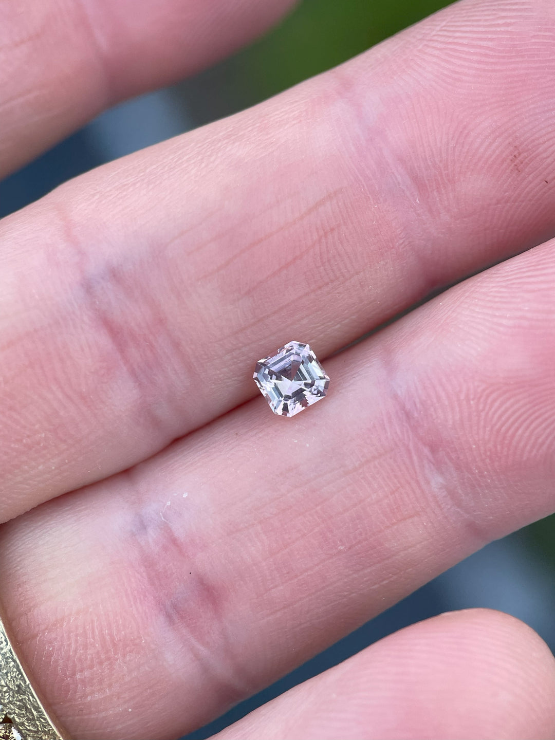 A natural, untreated Montana sapphire resting on a fingertip, showcasing its precise octagonal step cut and stunning pink hues.