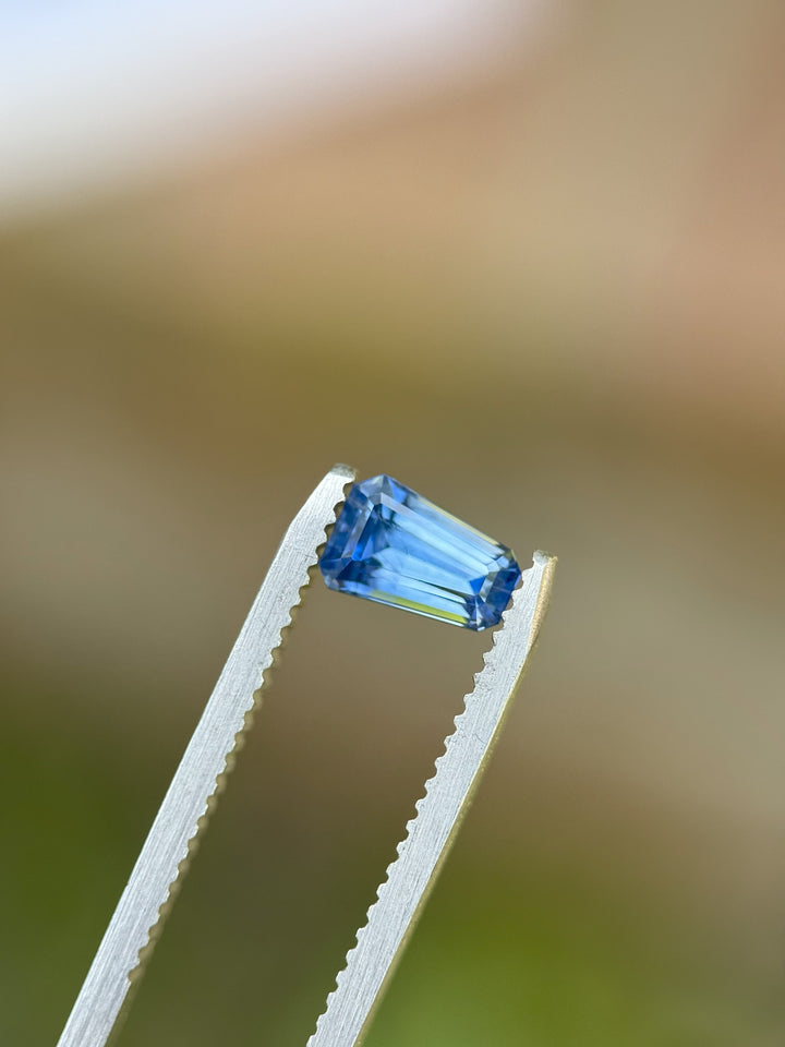 Close-up of 1.20CT blue sapphire from El Dorado Bar, Montana in tweezers, highlighting clean step cut facets and saturated blue tone.