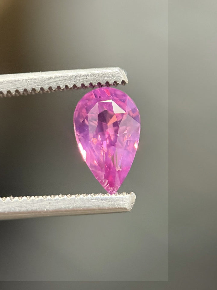 1.57ct pink sapphire in kite shape held in tweezers, highlighting facet brilliance and luster.