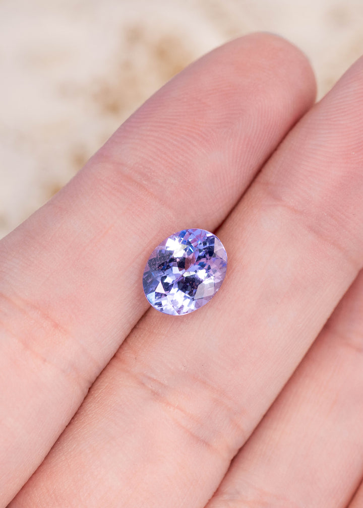 2.50 carat powder blue lavender violet Tanzanite resting on fingers showing custom mix brilliant oval faceting and vibrant color from Tanzania