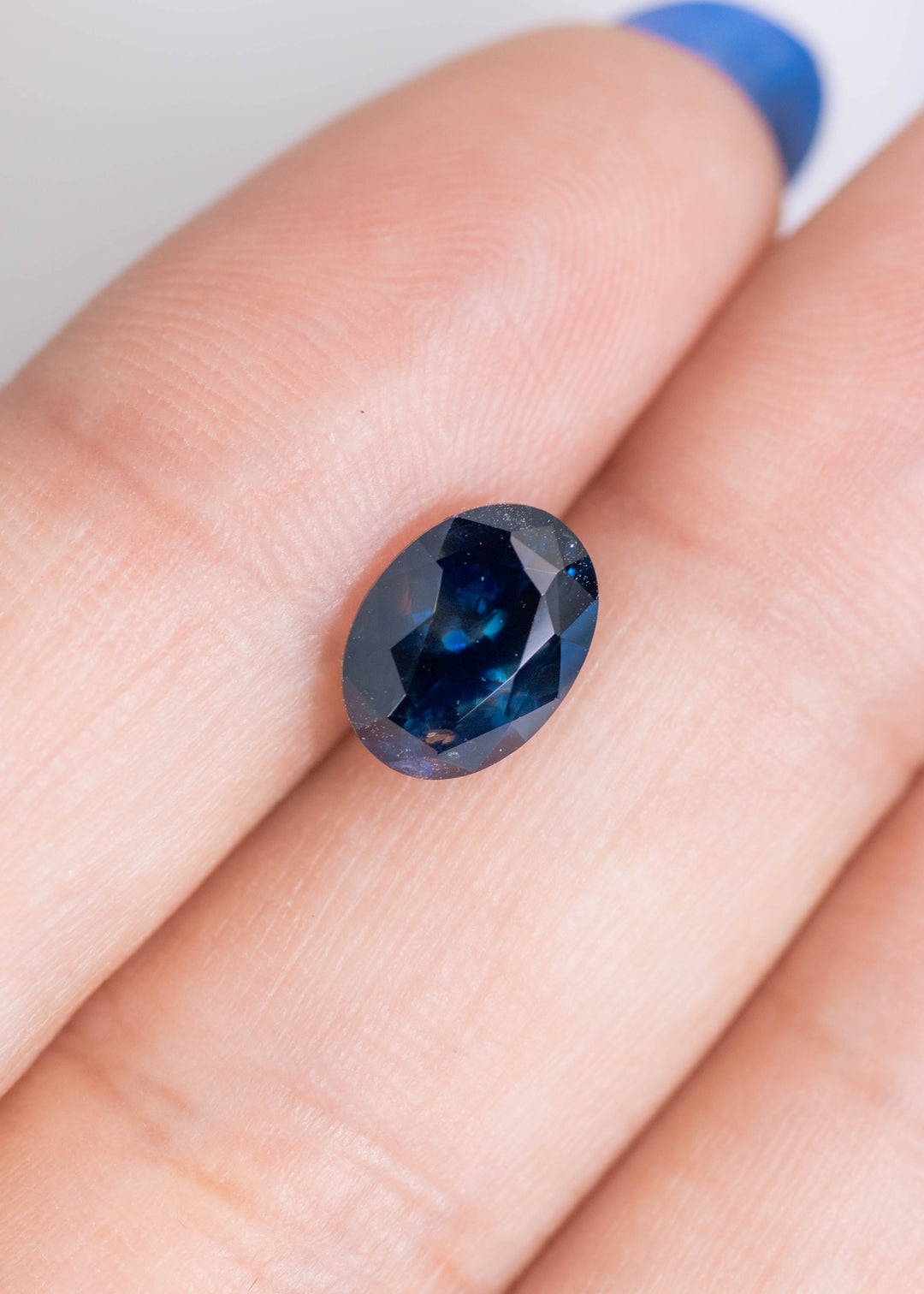 2.62 carat heated Montana blue sapphire oval mix cut displayed on finger for size reference, rich navy blue gemstone from El Dorado Bar Deposit, USA