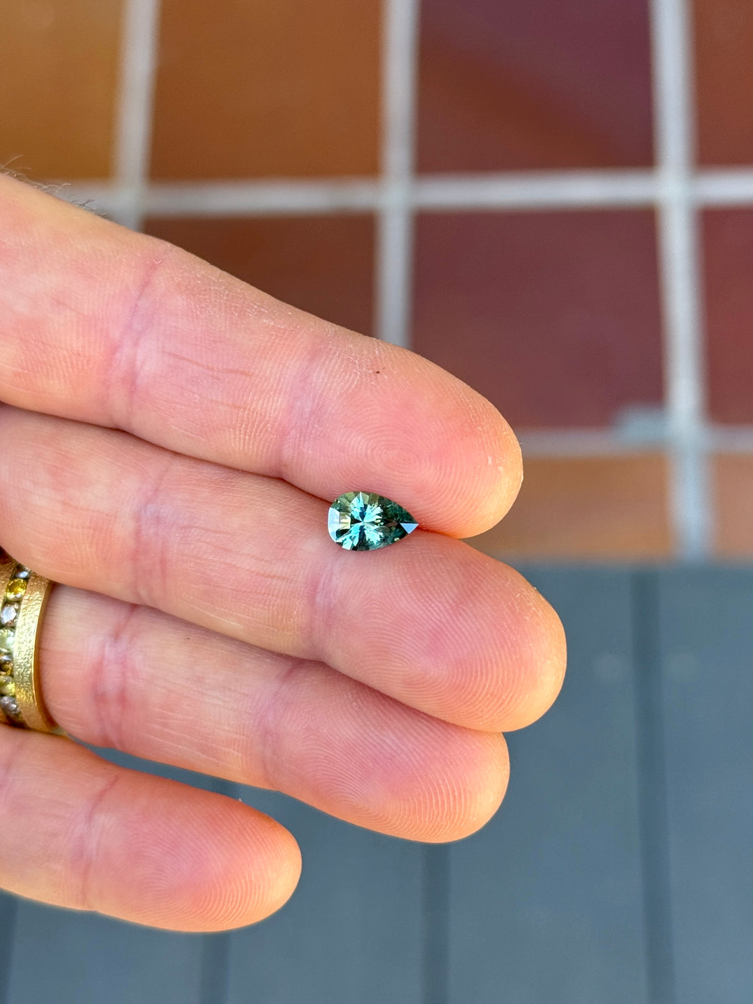 Lagoon teal green Montana sapphire displayed on fingers in natural light, showing a 1.34 carat heated shield step cut sapphire with bright teal sparkle and precision faceting.