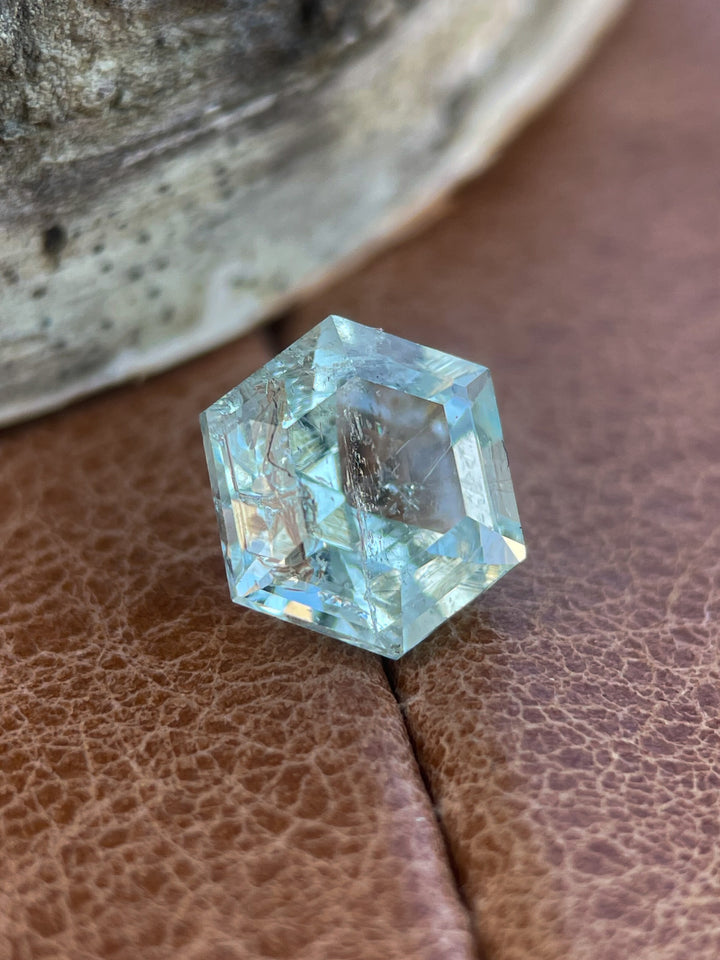 A close-up of a 2.20ct hexagon step-cut Green Beryl resting on a textured surface, emphasizing its clarity and natural brilliance.