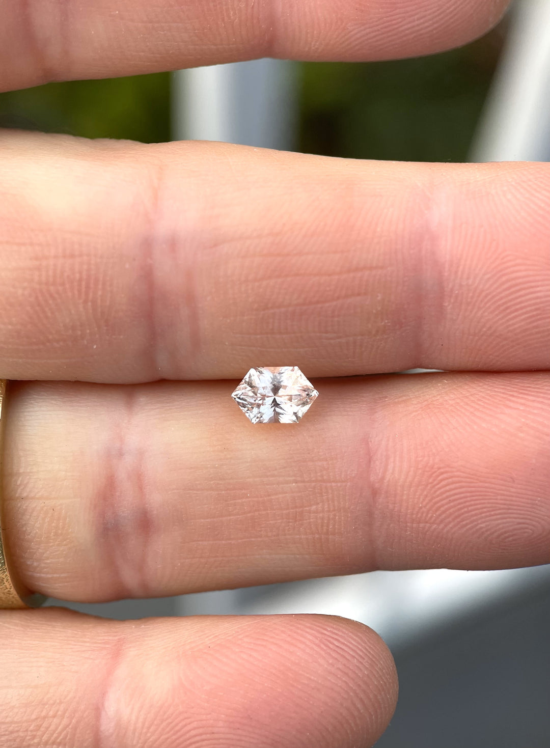 Hexagonal mix brilliant cut peach champagne sapphire, 1.06 carats, held between fingers, showcasing its clarity and light play.