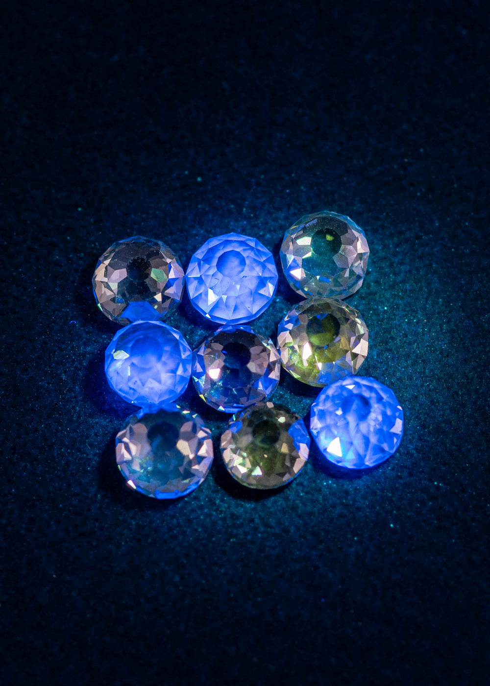 Mughal cut fancy light brown diamonds under UV light showing light blue fluorescence, highlighting antique faceting, open culets, and VVS clarity in a nine-piece diamond parcel