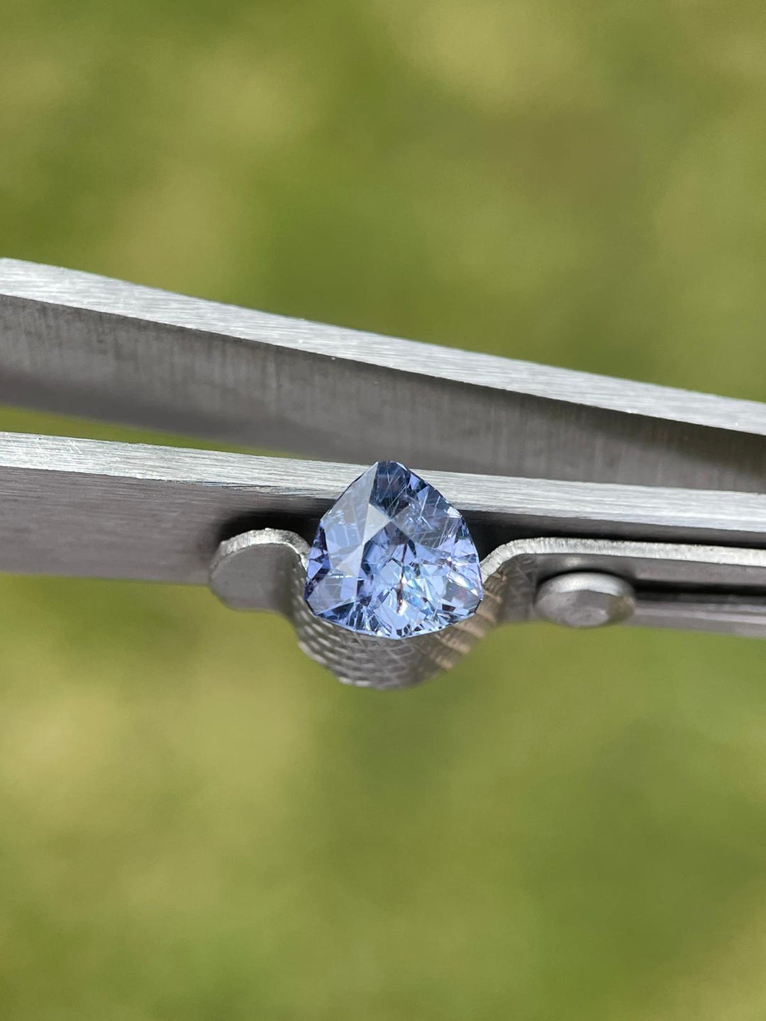 Elegant violet and denim sapphire gemstone, presented in tweezers with a focused background, emphasizing the gem's clarity and custom trillion cut.