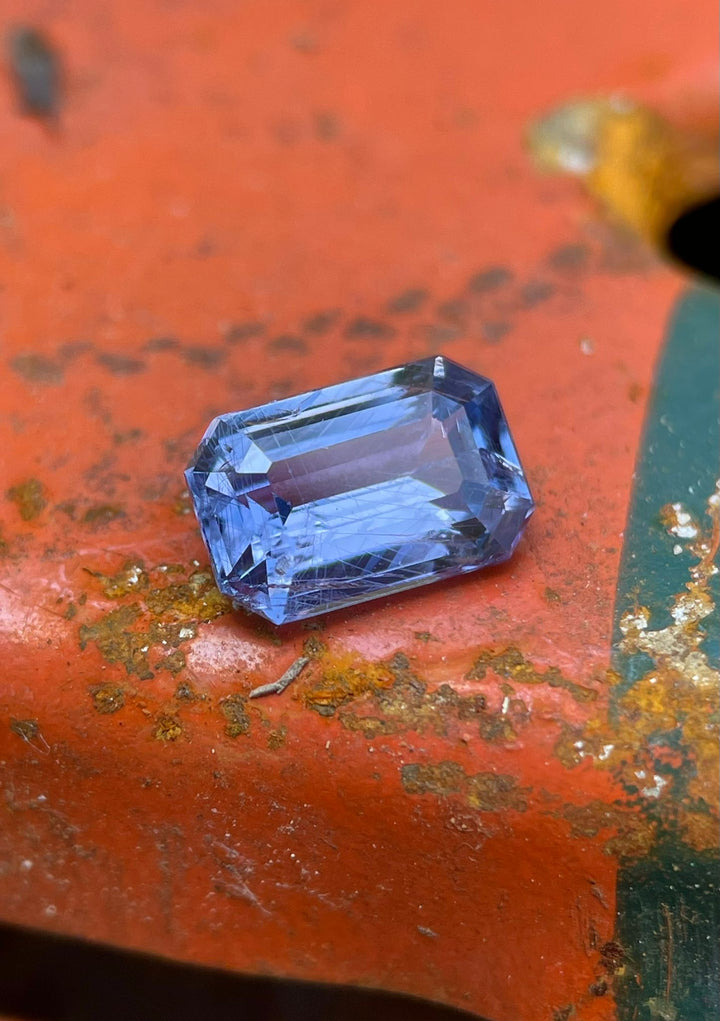 Close-up of a 1.26 carat violet-blue sapphire on a rusty surface, detailed view of its polished facets and deep blue tones, illustrating its untreated state and Tanzanian origin.