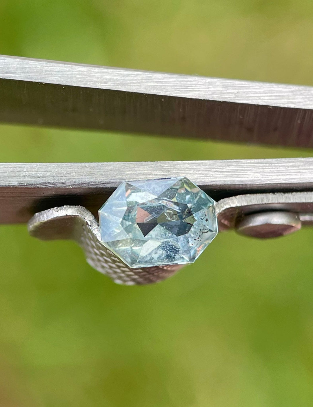 Custom octagonal radiant cut yellow and seafoam sapphire weighing 0.86 carats from Umba River, Tanzania, showcased between tweezer blades with a green background.