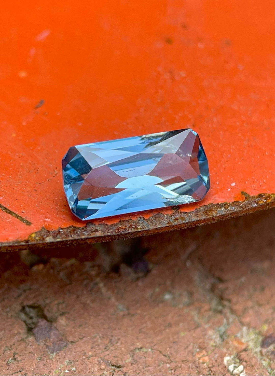 A striking blue sapphire positioned on a rustic orange and green surface. The gemstone's exquisite custom elongated geometric cushion cut and intense blue hue are captured in detail. Originating from the Umba River in Tanzania, this 1.26 carat, untreated sapphire is priced at $1197