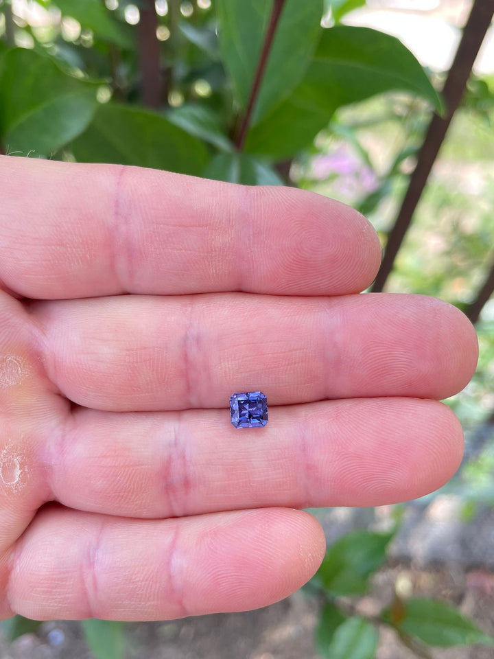 .68 carat violet and purple sapphire resting on a rustic, colorful painted surface, emphasizing its octagonal step cut and vibrant color depth.