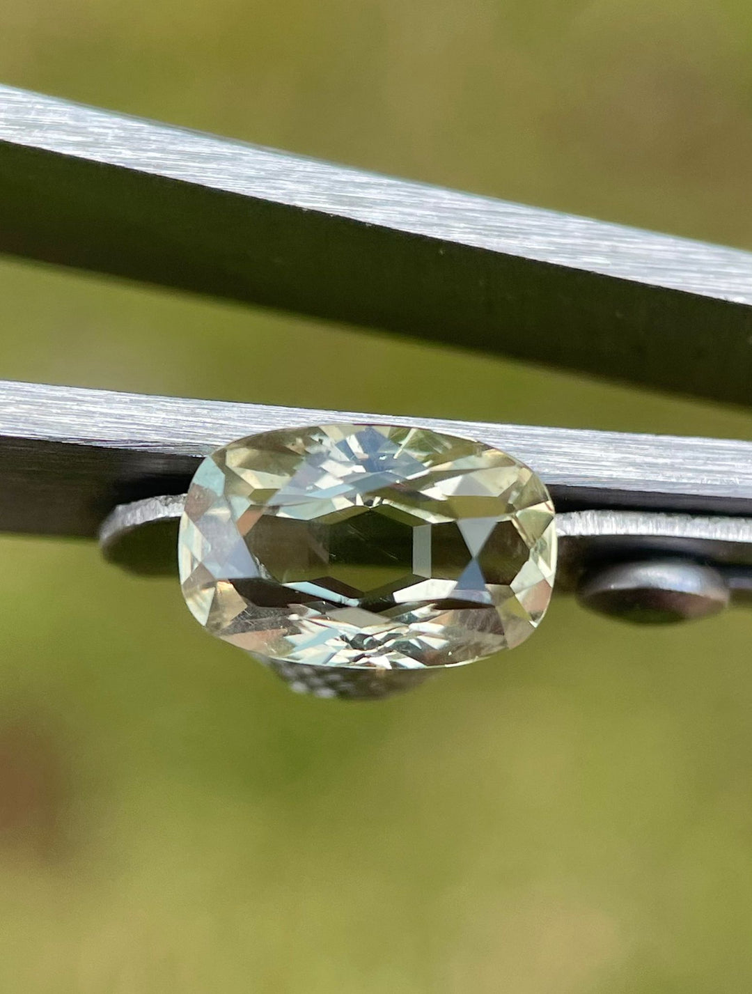 Detailed image of a 2.29-carat sapphire held by tweezers, emphasizing its unique modified cushion shape and multi-color depth with yellow, teal, and green shades, sourced from Umba River, Tanzania.