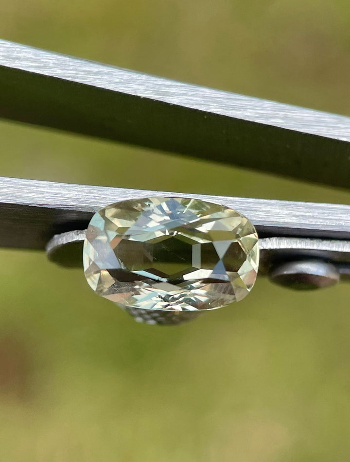 Detailed image of a 2.29-carat sapphire held by tweezers, emphasizing its unique modified cushion shape and multi-color depth with yellow, teal, and green shades, sourced from Umba River, Tanzania.