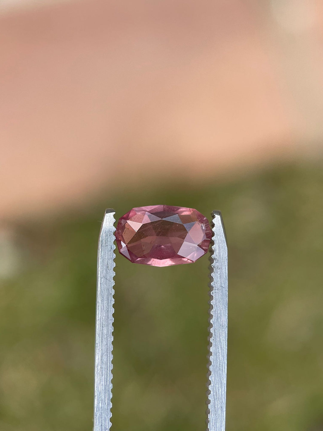 Elongated cushion cut sapphire, weighing 1.45 carats, resting on a rustic stone surface, highlighting its natural grapefruit and pastel colors.