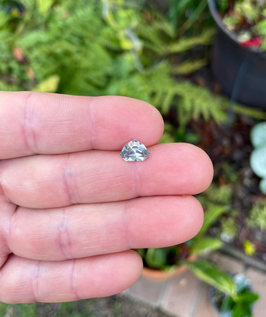 Sapphire gemstone from Umba River, Tanzania, displayed in hand with a focus on its custom shield cut and vibrant color transitions.