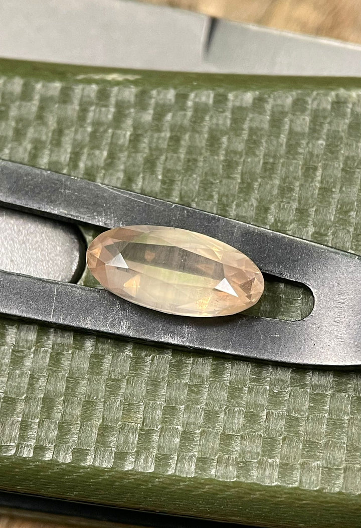 1.93 carat peach, opalescent sapphire held in tweezers over a green textured surface, highlighting its precise dimensions and natural, untreated quality.