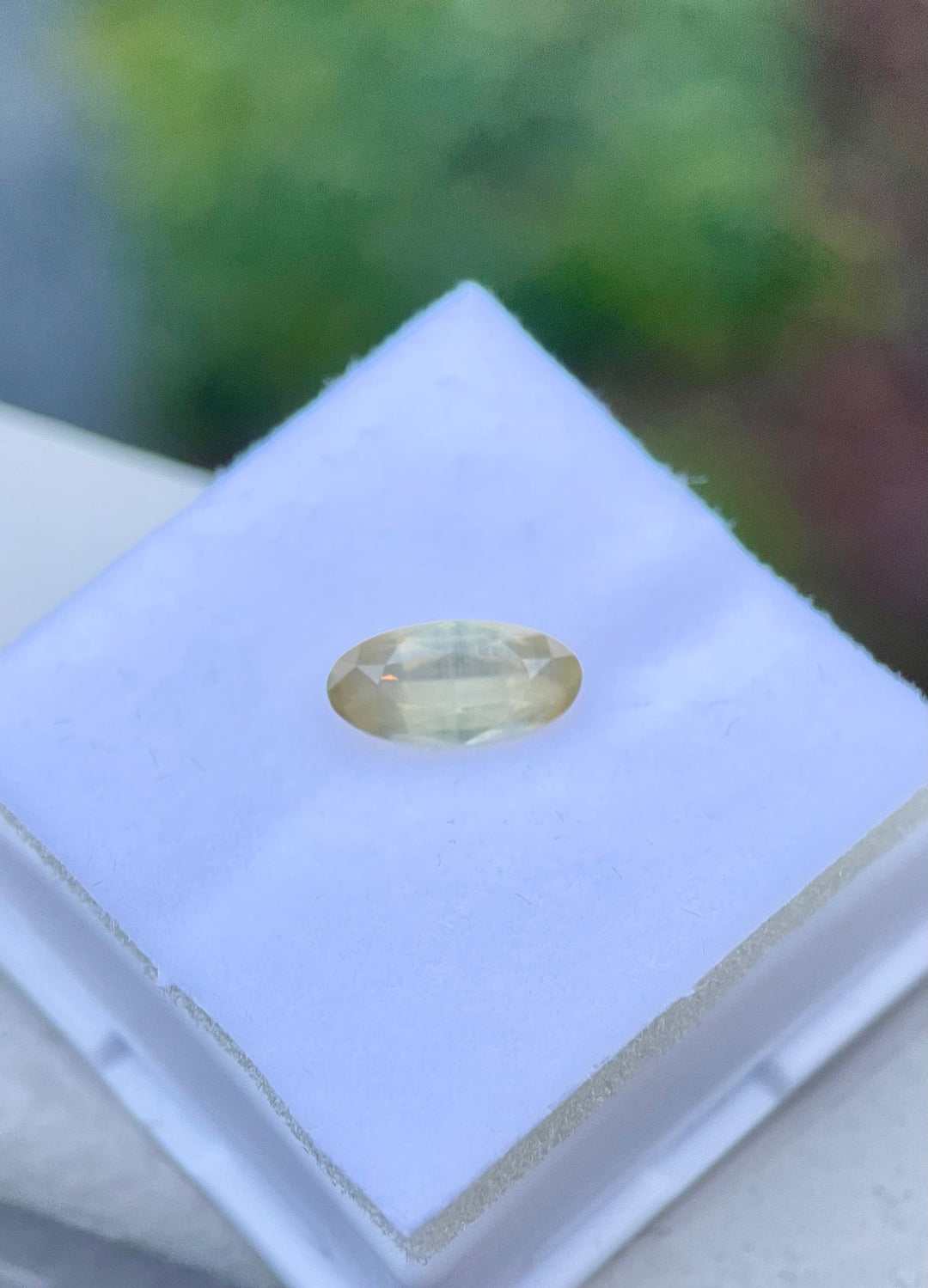 Close-up of a peach opalescent sapphire, displayed on a textured white foam pad, emphasizing the custom elongated oval cut and the gem's vibrant translucence.